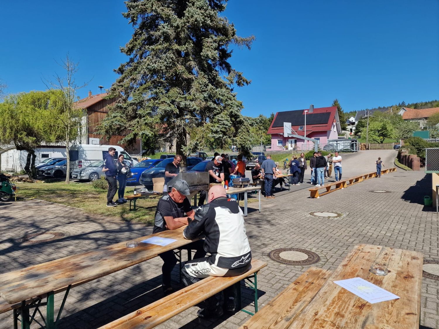 Besucher an Biertischgarnituren im Sonnenschein